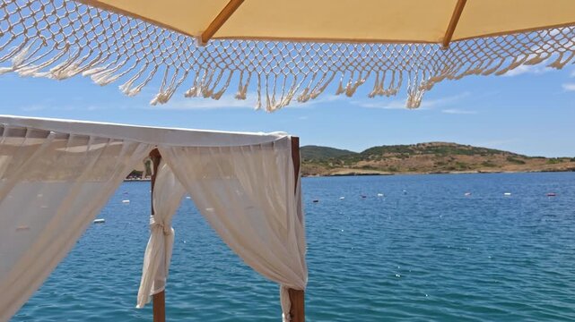 Beautiful 4K low-angle shot of white fringed macrame umbrellas at a luxury beach resort. Features an organized row of sunbeds, tropical palm trees, and a clear blue sky.