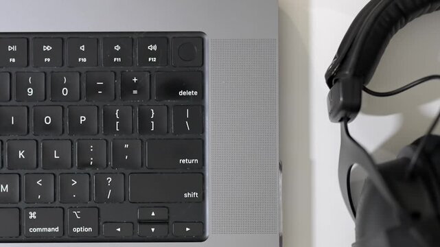 Close up laptop keyboard with headphones, smartphone, pan right to left