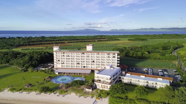 Aerial tracking view of a tropical beachside hotel resort with lush green surroundings and the ocean in Ishigaki Island, Okinawa, Japan.