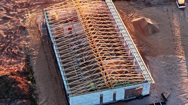 Home under construction with wooden roof trusses and concrete block walls in aerial view