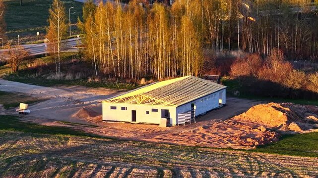 Aerial shot slowly approaching a building under construction with a wooden roof frame at sunset