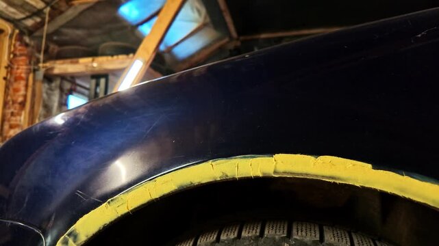 Detailed view of a dark blue car's fender and sill undergoing repair with yellow putty