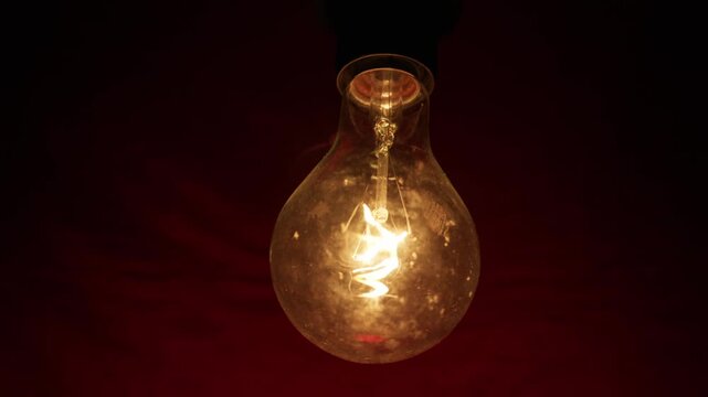 A vintage incandescent light bulb glows brightly against a dark textured background, revealing the burning filament inside the glass. Concept of creativity, innovation, and inspiration.