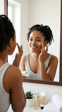 Young African American woman applying face cream morning skincare routine mirror reflection and beauty products home healthy glowing skin relaxing spa mood self care beauty ritual natural wellness