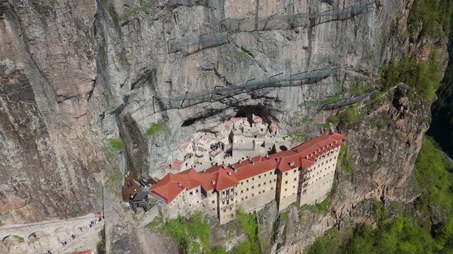 Wide aerial view of the historic Sumela Monastery built into a steep cliff face in the Pontic Mountains. Famous greek orthodox landmark surrounded by green forest valleys in Turkey.