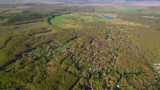 High drone shot across a forested rural village with scattered homes spring trees fields and open countryside for residential nature and regional landscape themes