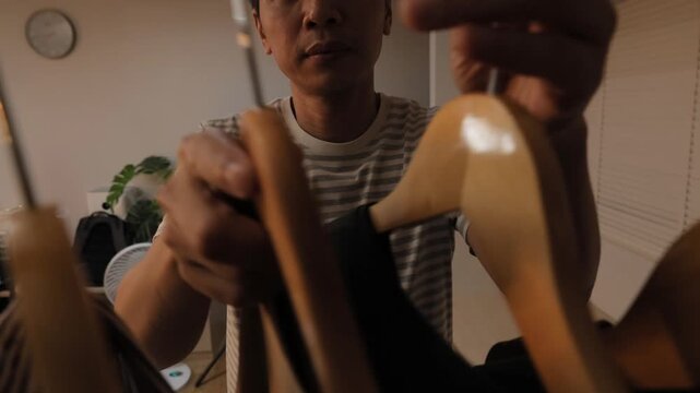 Close-up of a man holding wooden hangers and organizing his wardrobe, sorting or choosing clothes in his closet at home.