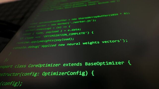 Green lines of programming code are displayed on a dark computer monitor with shallow focus. Concept of modern software development, artificial intelligence, and digital cybersecurity.