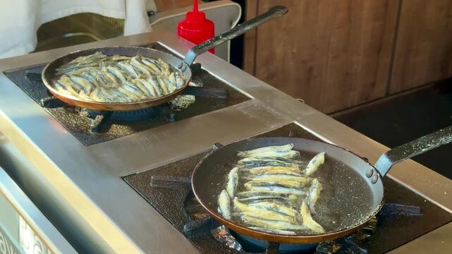 A commercial video of fresh European anchovies (hamsi) frying in a hot pan. The small fish are tightly and neatly arranged in a traditional circular pattern, cooking to a golden crisp