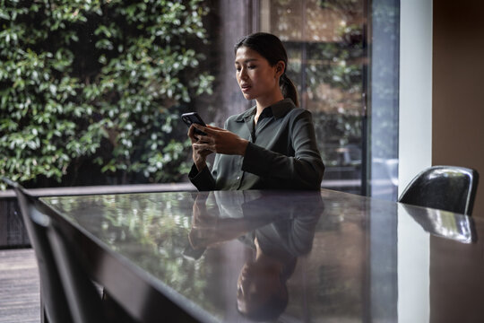 Businesswoman using her phone in an empty meeting room