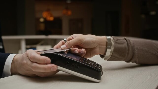 Cropped shot of female guest paying with credit card at hotel reception desk, tapping card on terminal and entering PIN code. Clip is ideal for banking, and contactless payment commercials