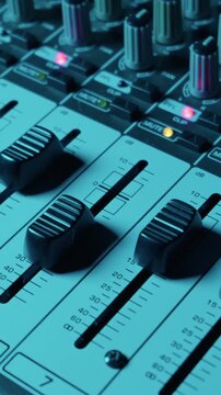 A close-up view shows the faders and control knobs of a professional audio mixing console in warm lighting. This represents high-quality music production and professional sound engineering.
