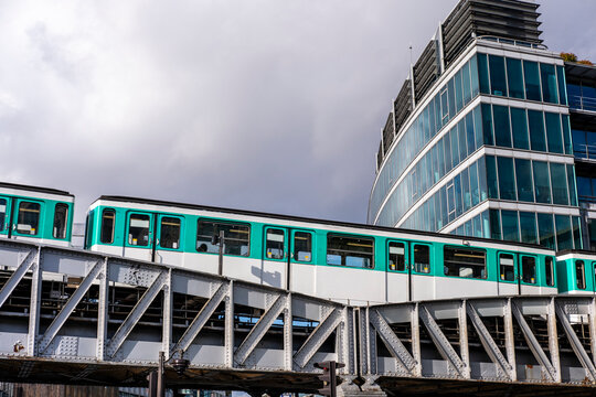 Green metro train runs across an elevated bridge in Paris, with France railway tracks, urban architecture and station structure beneath a cloudy sky