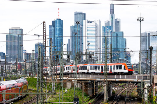 Frankfurt skyline rises beyond red train tracks and station infrastructure, showing Germany railway lines and urban towers through a layered transit corridor