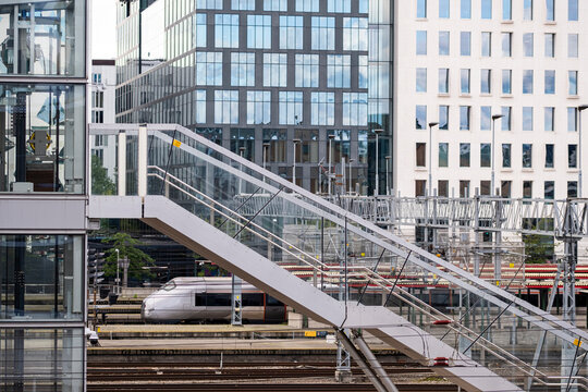 White train crosses below a glass bridge near Oslo station, with railway tracks, platform edges and Norway urban infrastructure framed by office buildings