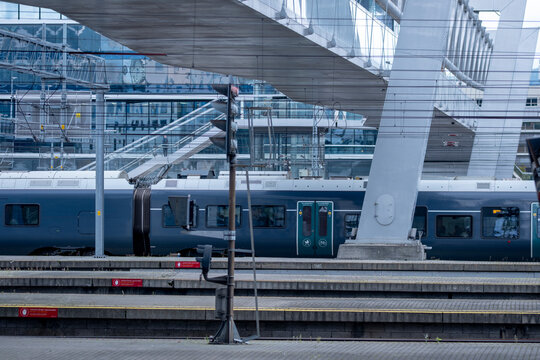 Blue train beside a quiet platform at Oslo station, seen through glass and bridge supports as Norway railway infrastructure forms a precise transit scene