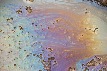 Fototapeta premium Iridescent oil slick patterns swirling on melting spring slush, toxic chemical residue and gasoline stains creating vibrant rainbow texture on wet asphalt surface, environmental pollution concept