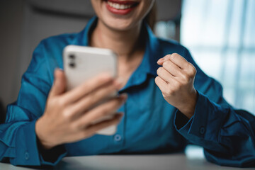 Fototapeta premium Happy Woman Celebrating Good News on Smartphone at Home Office. Success notification, financial achievement, happiness, digital lifestyle