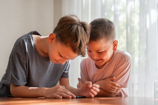 Two boys using a smartphone together, exploring content looking at screen phone at home. Generation Alpha childhood, digital literacy, curiosity, social interaction and shared learning experience