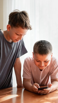 Young boys using smartphone together in bright home environment. Concept of peer learning, educational technology, Generation Alpha and modern childhood.