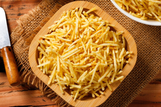Portion of golden shoestring potatoes served on a rustic wooden serving platter, accompanied by an antique knife and burlap cloth