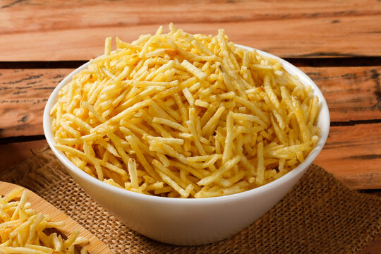 Portion of golden potato sticks inside a white ceramic bowl with burlap fabric at the bottom