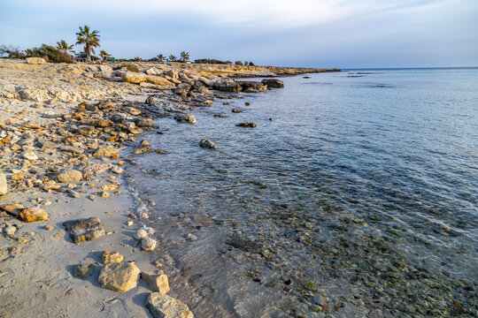 Calm sea water on rocky sandy shore near famous Landa beach area under cloudy sky in evening light. Quiet marine coastal landscape during low season, Ayia Napa region, Cyprus.