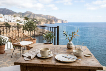 Obraz premium Coastal terrace breakfast table by the sea with ceramic tableware and a vase for summer balcony background and travel lifestyle