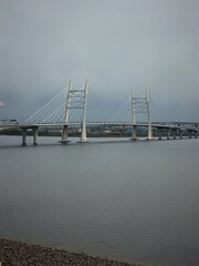 Obraz premium Large white cable stayed bridge spanning across the wide river water under a gloomy cloudy sky