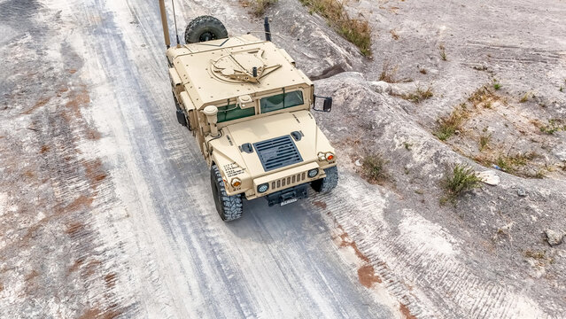 Military vehicle moves on dirt road in a training area during daylight hours