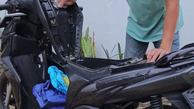 Motorcycle owner cleans motorcycle trunk using chamois cloth outdoors