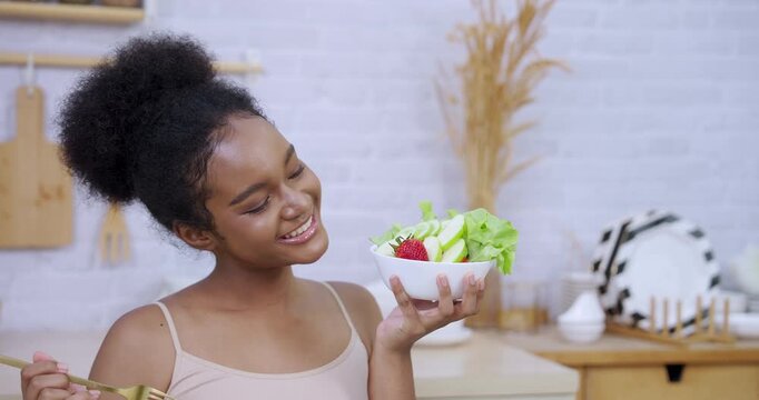 Smiling african teenage girl looking delighted while holding fork and salad bowl enjoying fresh vegetables strawberries representing clean food healthy lifestyle skin glow slowmotion joy