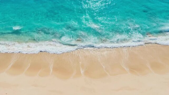 Aerial view of a pristine tropical beach with turquoise ocean waves gently lapping the golden sand.