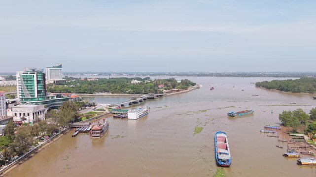 Boat Carrying Goods Along Riverfront. Modern Boat Crew Navigating Muddy River Waters Towards Urban Quay. An Asian Crew Operates Cargo Boat Along Muddy River Towards Vibrant City Shore