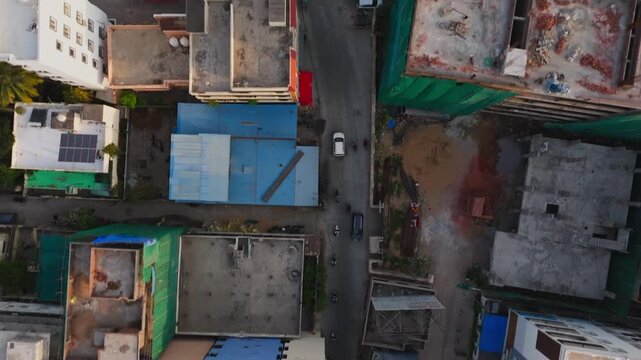 vehicles moving on narrow road with under construction building and residential buildings terrace at Shirdi Sai Nagar, manikonda, hyderabad, india. day time, trucking shot, top down, drone shot, 4k.