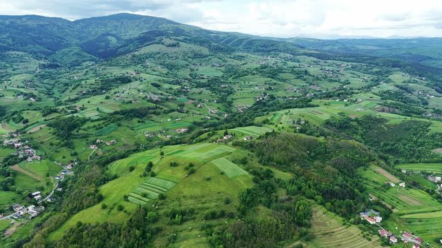 Beautiful aerial drone footage of rural countryside in central Slovakia featuring scattered villages, patchwork farmland, rolling green hills and forested mountains. Authentic Slovak landscape in summ
