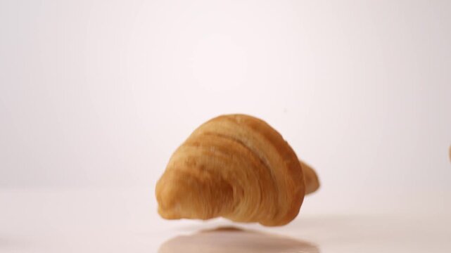 Golden buttery flaky croissants dropping and bouncing across white seamless backdrop in high speed slow motion. european cafe ads, mothers day brunch posts, sunday breakfast content.