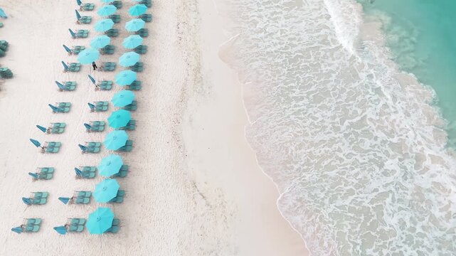drone view of a neat row of umbrellas on the white sand of Carlisle Bay beach, ocean waves rolling onto the shore in Bridgetown, tropical resort destination, Barbados