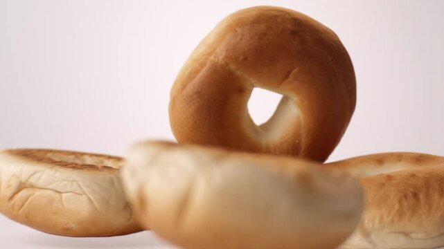 Chewy golden bagels bouncing and tumbling on white in slow motion macro studio shot. new york deli content, bagel shop branding, brunch menu reels.