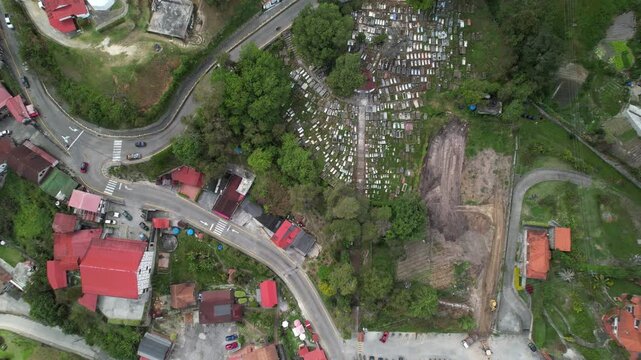 Aerial tilt-up over Colonia Tovar, Venezuela, revealing charming red-roofed houses, tropical mountain region, and vehicles traveling through the village at sunset