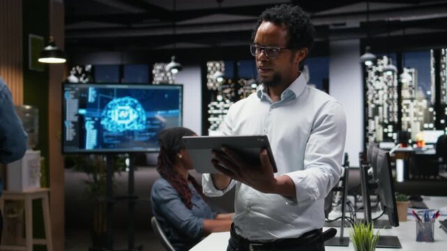 Engineer in office using tablet, working to fix bugs in AI system. IT worker troubleshooting neural network errors with device in tech agency workplace.