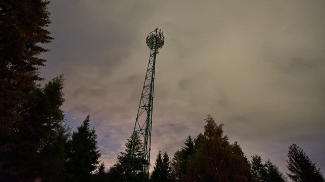 Night Timelapse of Telecommunications Tower Above Forest Under Cloudy Sky