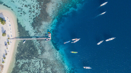 Obraz premium Top Down Aerial View of Wooden Jetty, Sandy Beach and Coral Reef at Kanawa Island