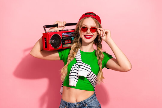 Young stylish woman with red cap and green crop top poses with a retro red boombox