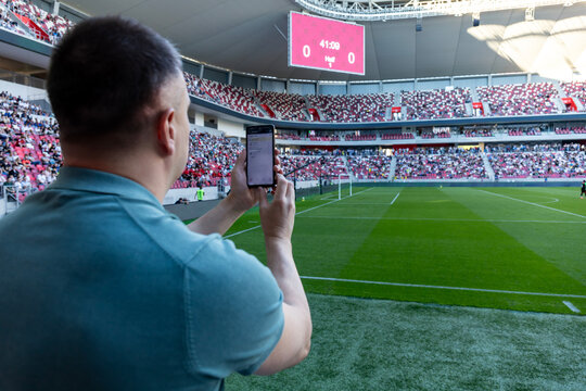 Caucasian man holding smartphone with sports bets app while watching football in the stadium