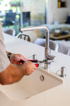 Man fixing kitchen sink faucet with wrench