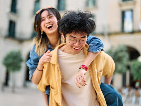 Portrait of a lovely young couple having fun and laughing together piggyback outdoors, tourists travel in the city