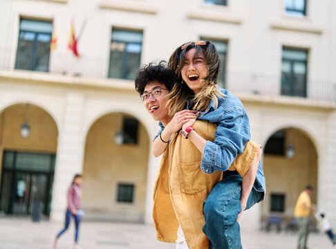 Portrait of a lovely young couple having fun and laughing together piggyback outdoors, tourists travel in the city