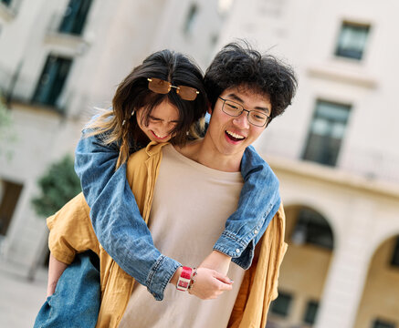 Portrait of a lovely young couple having fun and laughing together piggyback outdoors, tourists travel in the city