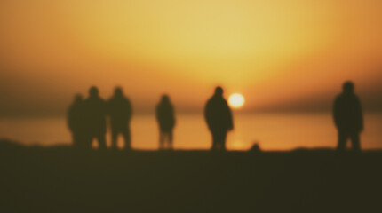 Fototapeta premium Blurry figures of friends or travelers by the water watching the sunrise on a sandy beach